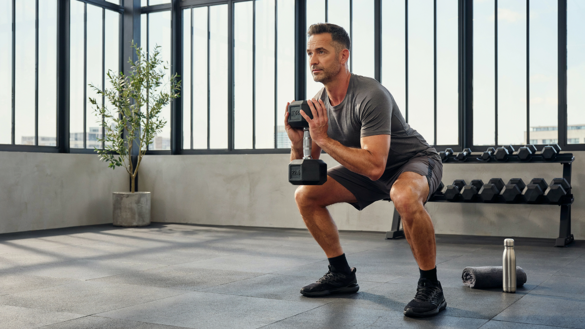 Hombre de 40 años ejecutando sentadilla goblet con mancuerna en home gym para proteger la columna y ganar fuerza